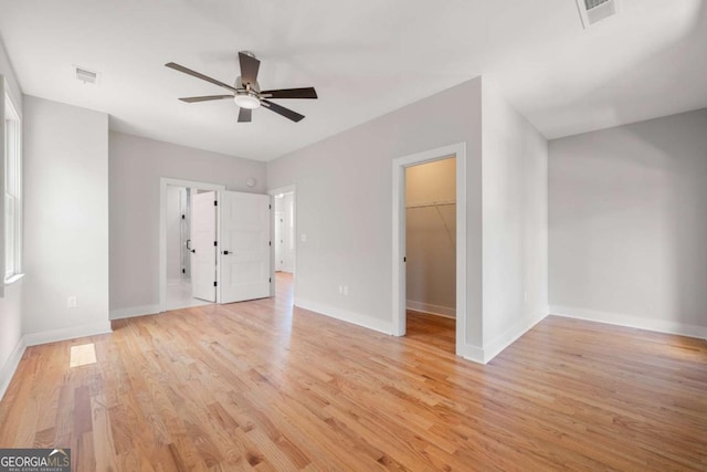 unfurnished bedroom featuring a walk in closet, ceiling fan, a closet, and light hardwood / wood-style flooring