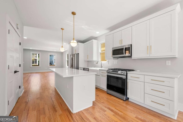 kitchen featuring white cabinetry, stainless steel appliances, light hardwood / wood-style flooring, pendant lighting, and a kitchen island