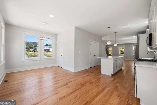 kitchen featuring stainless steel refrigerator, hanging light fixtures, light hardwood / wood-style floors, a kitchen island with sink, and white cabinets