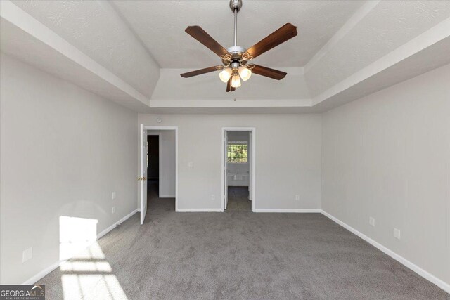 unfurnished bedroom featuring a raised ceiling, ensuite bath, ceiling fan, a textured ceiling, and carpet floors