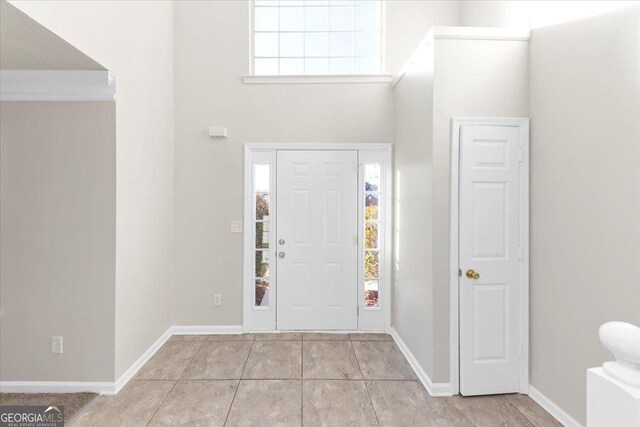 entrance foyer featuring a towering ceiling, light tile patterned floors, and ornamental molding
