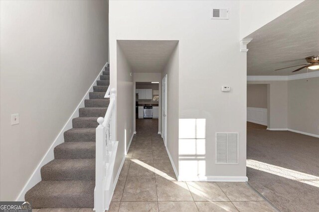 stairway with ceiling fan, crown molding, and carpet floors