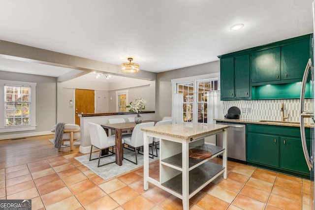 kitchen featuring backsplash, light stone countertops, green cabinetry, light tile patterned flooring, and stainless steel dishwasher