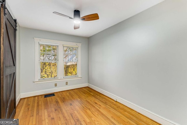 unfurnished room with light hardwood / wood-style floors, a barn door, and ceiling fan