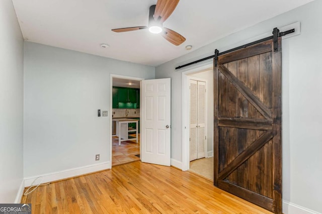 unfurnished bedroom with ceiling fan, a barn door, light wood-type flooring, and a closet