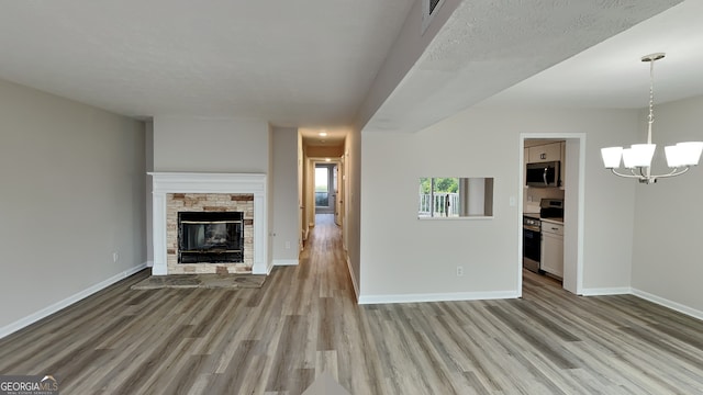 unfurnished living room featuring a textured ceiling, light wood-type flooring, a fireplace, and an inviting chandelier