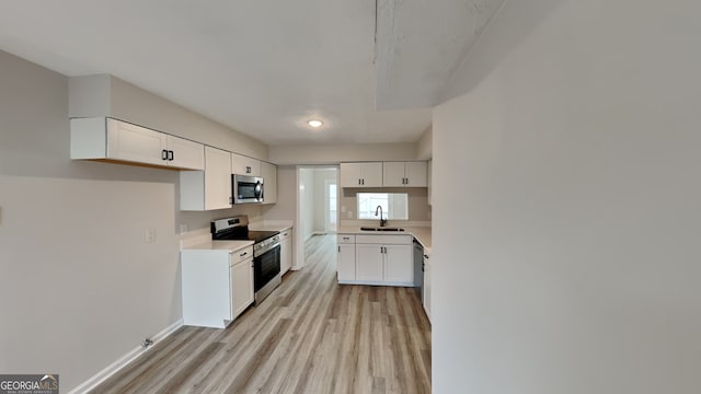 kitchen with sink, white cabinetry, stainless steel appliances, and light hardwood / wood-style flooring