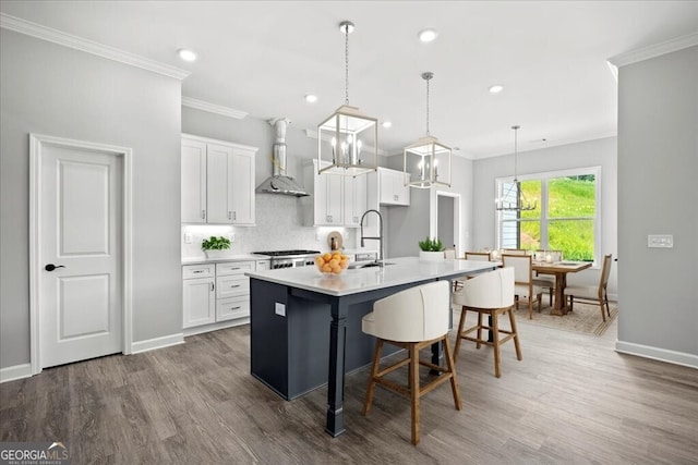 kitchen featuring white cabinetry, a kitchen island with sink, pendant lighting, wall chimney exhaust hood, and a breakfast bar