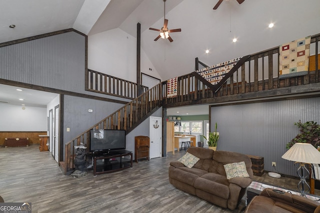 living room featuring wooden walls, ceiling fan, wood-type flooring, and high vaulted ceiling