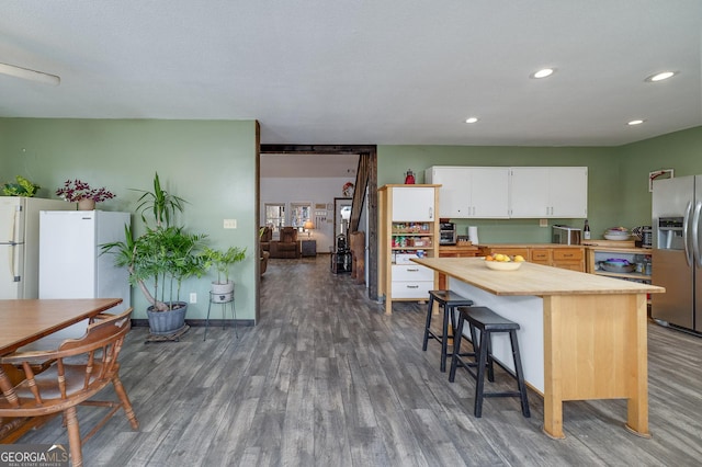 kitchen featuring wooden counters, dark hardwood / wood-style floors, stainless steel fridge, a breakfast bar, and white cabinets