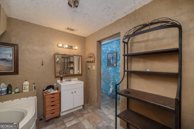 bathroom featuring a tub to relax in, vanity, and a textured ceiling