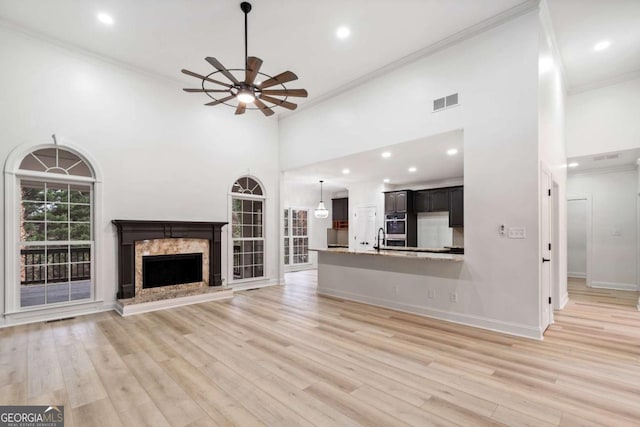 unfurnished living room featuring a towering ceiling, light wood-type flooring, ornamental molding, and a premium fireplace