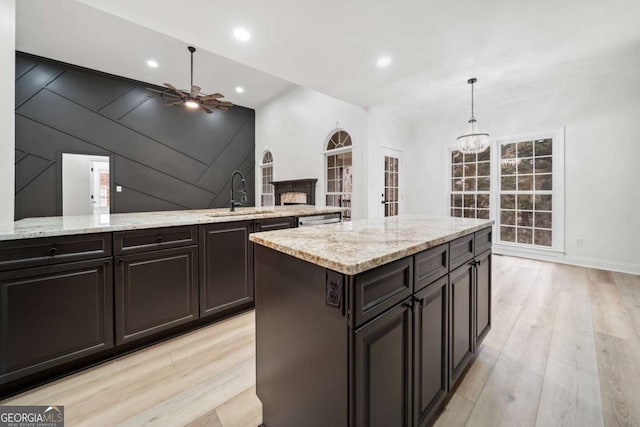 kitchen featuring light stone counters, sink, pendant lighting, and light hardwood / wood-style flooring