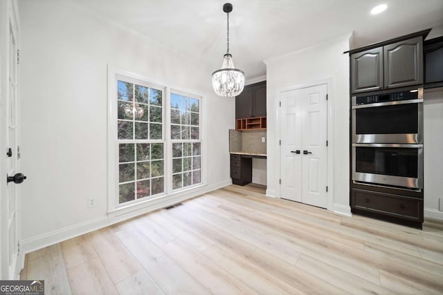 kitchen featuring double oven, backsplash, light hardwood / wood-style floors, and an inviting chandelier