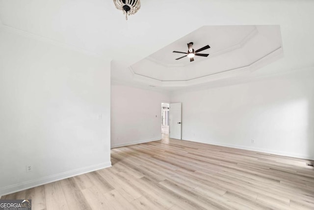 empty room with a raised ceiling, crown molding, ceiling fan, and light hardwood / wood-style floors