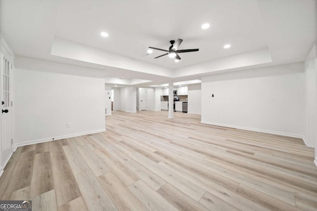 unfurnished living room featuring light hardwood / wood-style floors, ceiling fan, and a tray ceiling