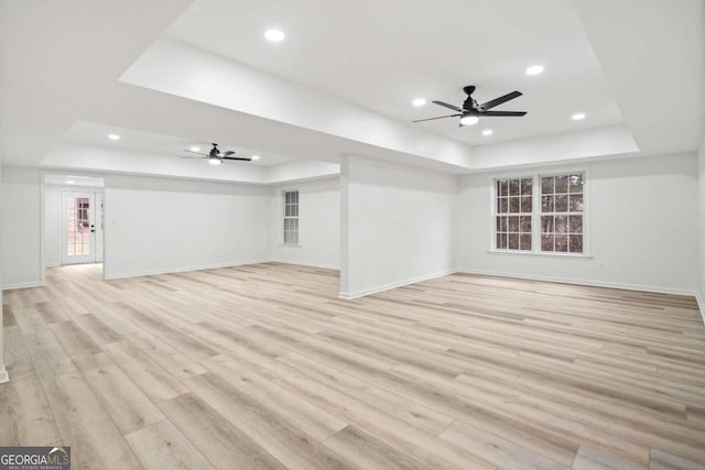 unfurnished living room featuring a raised ceiling, ceiling fan, and light hardwood / wood-style floors