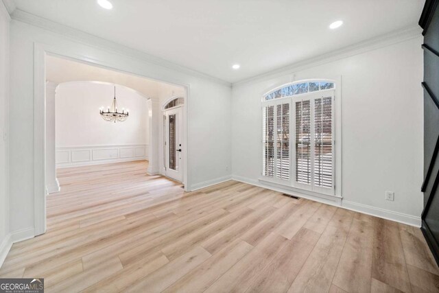 spare room featuring a chandelier, light hardwood / wood-style floors, and crown molding