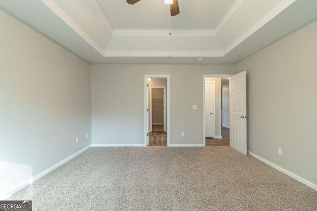 unfurnished bedroom featuring carpet, ceiling fan, a walk in closet, and a tray ceiling