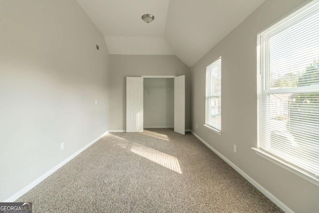 unfurnished bedroom with carpet flooring, vaulted ceiling, and multiple windows