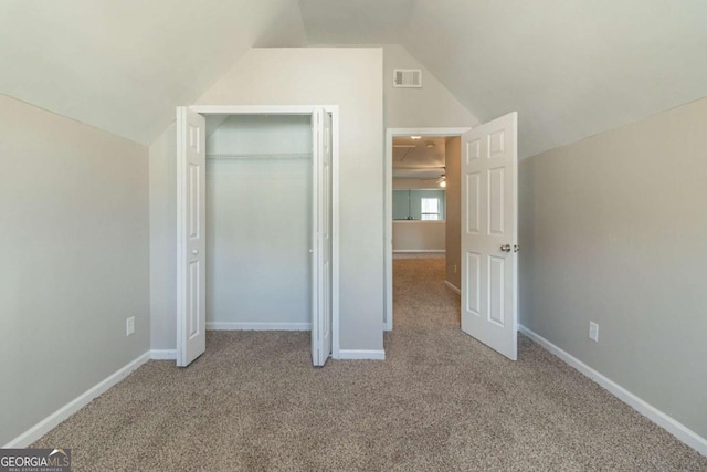 unfurnished bedroom with light colored carpet, a closet, and lofted ceiling