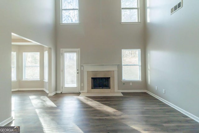 unfurnished living room with a wealth of natural light, dark hardwood / wood-style flooring, and a towering ceiling