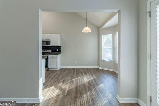 kitchen with lofted ceiling, hanging light fixtures, tasteful backsplash, white cabinetry, and stainless steel appliances