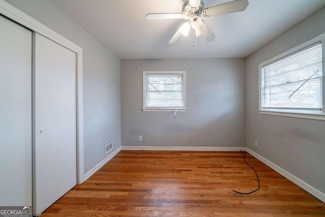 unfurnished bedroom with multiple windows, ceiling fan, a closet, and wood-type flooring