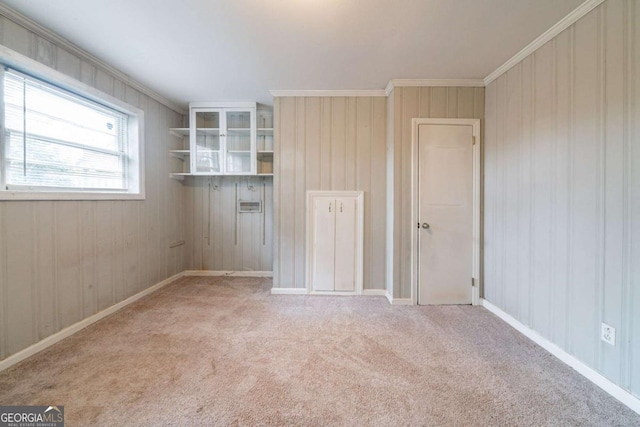 carpeted spare room featuring crown molding and wooden walls