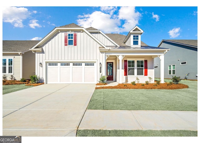 view of front facade featuring board and batten siding, a front yard, concrete driveway, and roof with shingles