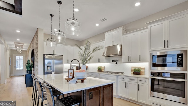 kitchen featuring pendant lighting, stainless steel appliances, white cabinetry, and a center island with sink