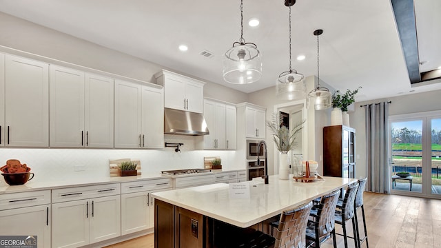 kitchen with white cabinetry, light hardwood / wood-style floors, decorative light fixtures, a kitchen bar, and a kitchen island with sink