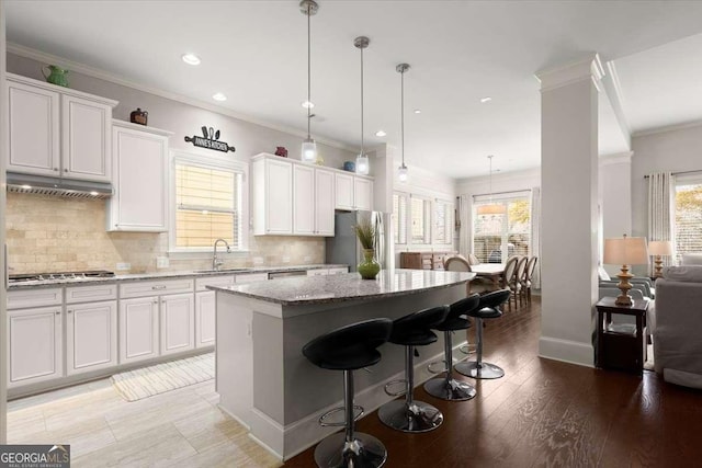 kitchen with light stone counters, stainless steel appliances, pendant lighting, a center island, and white cabinetry