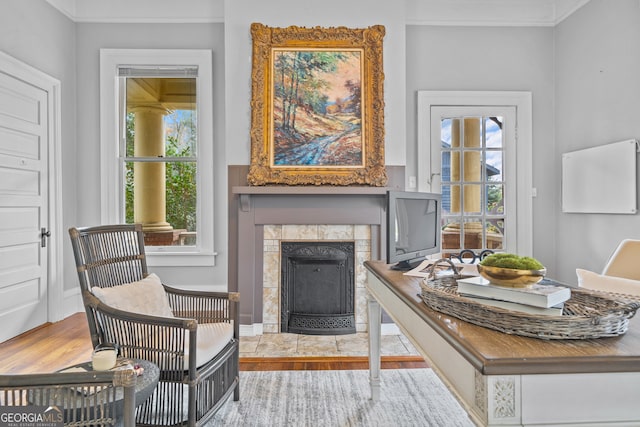 living area featuring a tiled fireplace, ornamental molding, and light wood-type flooring