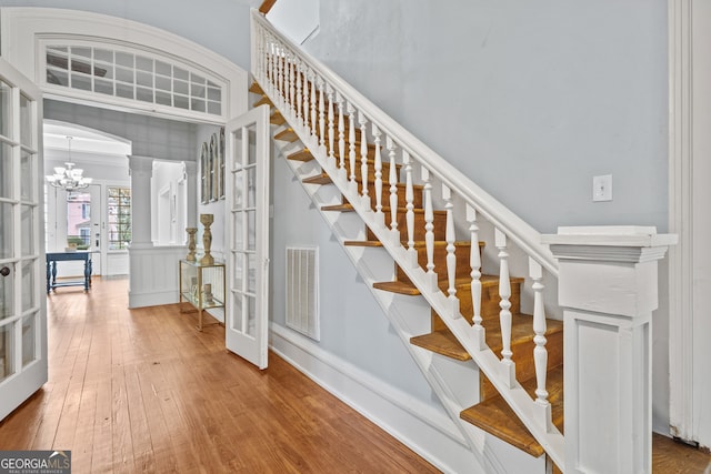 staircase featuring french doors, ornate columns, a notable chandelier, and wood-type flooring