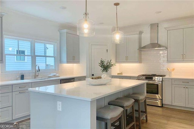 kitchen with sink, stainless steel appliances, wall chimney range hood, a kitchen island, and light wood-type flooring