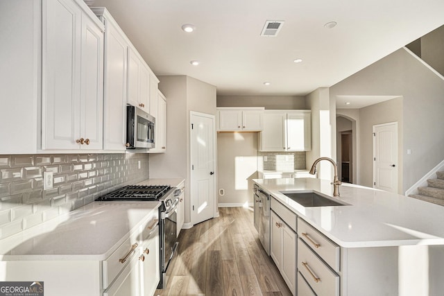 kitchen featuring white cabinets, sink, an island with sink, appliances with stainless steel finishes, and light hardwood / wood-style floors