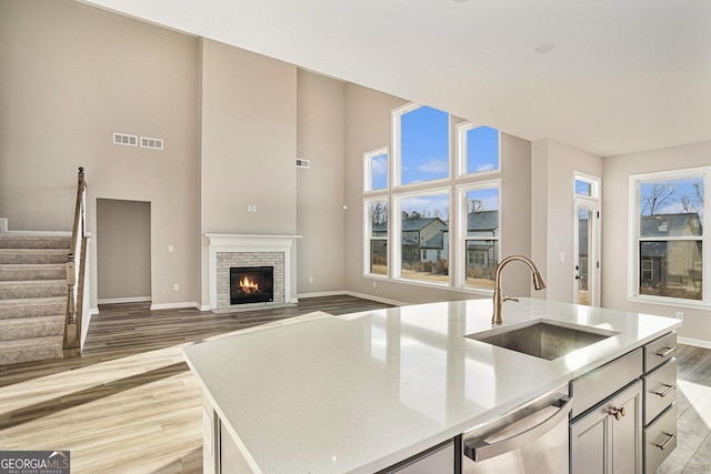 kitchen featuring light wood-type flooring, a center island with sink, a brick fireplace, and sink