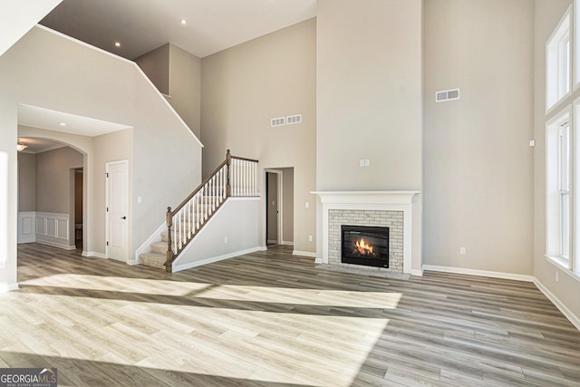 unfurnished living room featuring a brick fireplace, a towering ceiling, and light hardwood / wood-style flooring