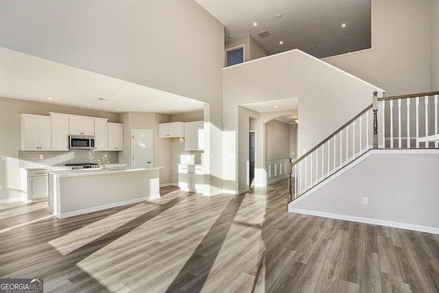 kitchen with white cabinetry, tasteful backsplash, a towering ceiling, light hardwood / wood-style floors, and a center island with sink