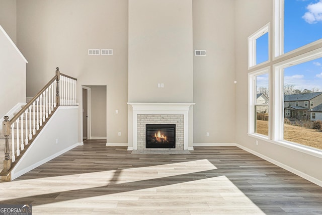 unfurnished living room featuring hardwood / wood-style floors, a brick fireplace, and a high ceiling