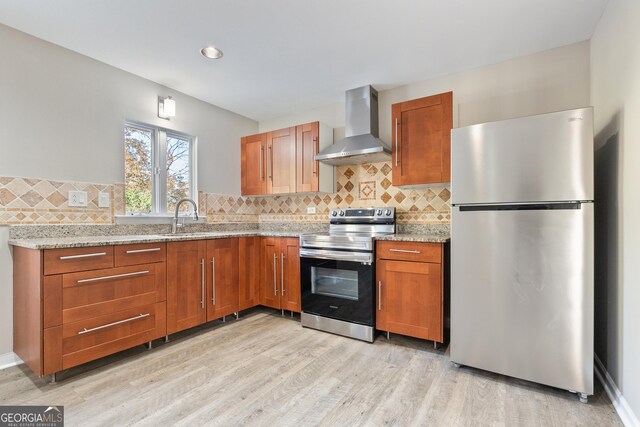 kitchen featuring light stone countertops, sink, wall chimney exhaust hood, light hardwood / wood-style flooring, and appliances with stainless steel finishes