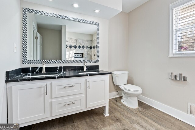 bathroom featuring a tile shower, hardwood / wood-style flooring, vanity, and toilet