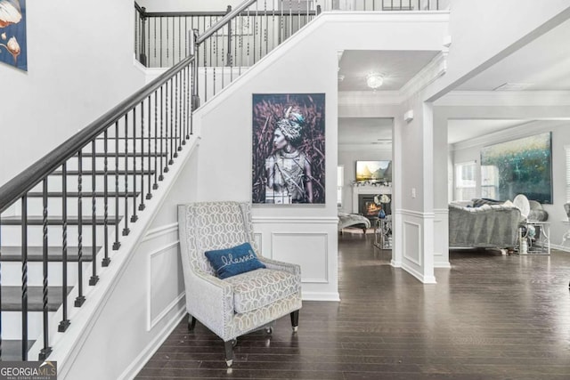 stairway with a glass covered fireplace, wood finished floors, a decorative wall, and crown molding