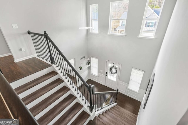 stairs with wainscoting, a decorative wall, a high ceiling, and wood finished floors