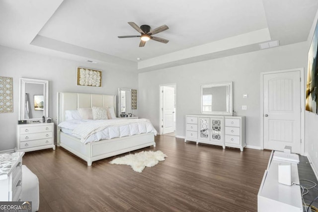 bedroom featuring a tray ceiling, baseboards, dark wood-style floors, and ceiling fan