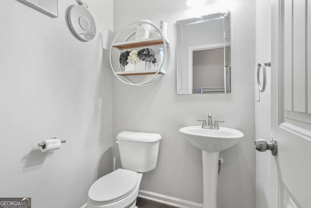 half bath with toilet, baseboards, and a sink