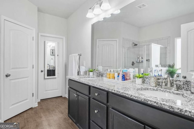 bathroom featuring wood finished floors, a sink, a stall shower, double vanity, and visible vents