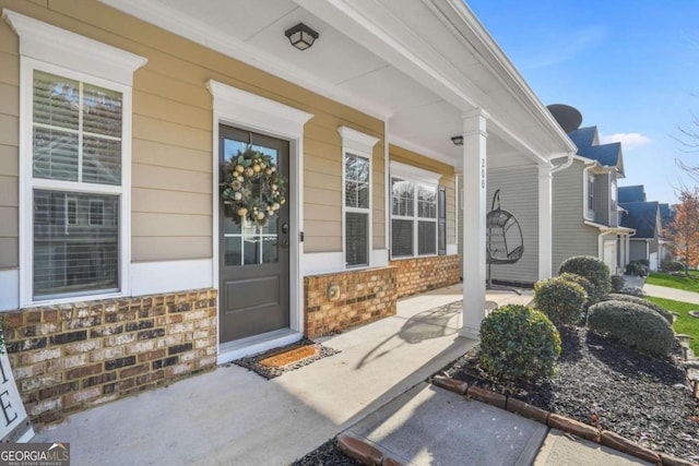 view of exterior entry featuring a porch and brick siding