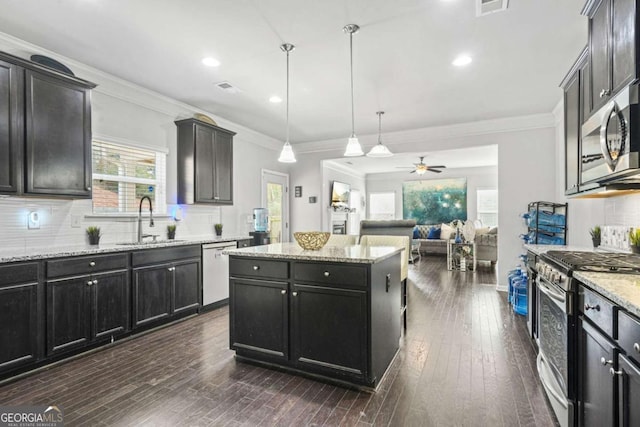 kitchen featuring stainless steel appliances, a kitchen island, a sink, open floor plan, and hanging light fixtures